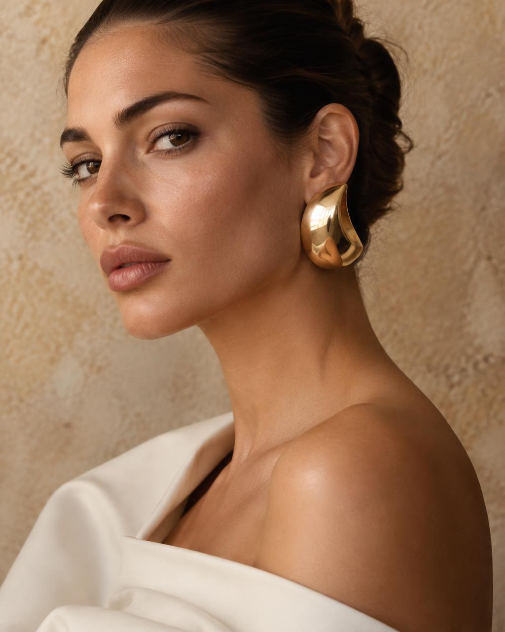 Woman wearing a large sculptural gold earring, shown in profile.